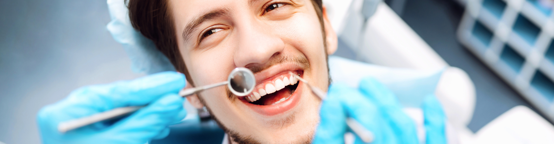 Gloved hands using dental tools in man's mouth.